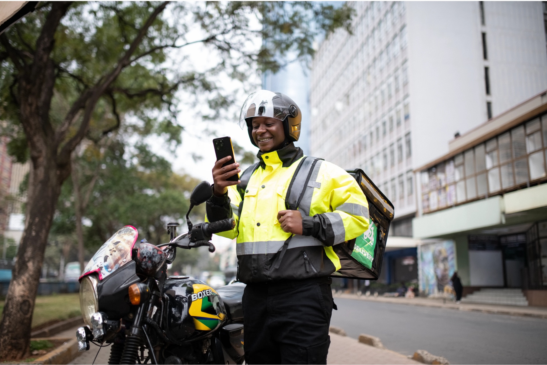 Original street photograph of a delivery rider checking his phone beside his motorbike in Nairobi