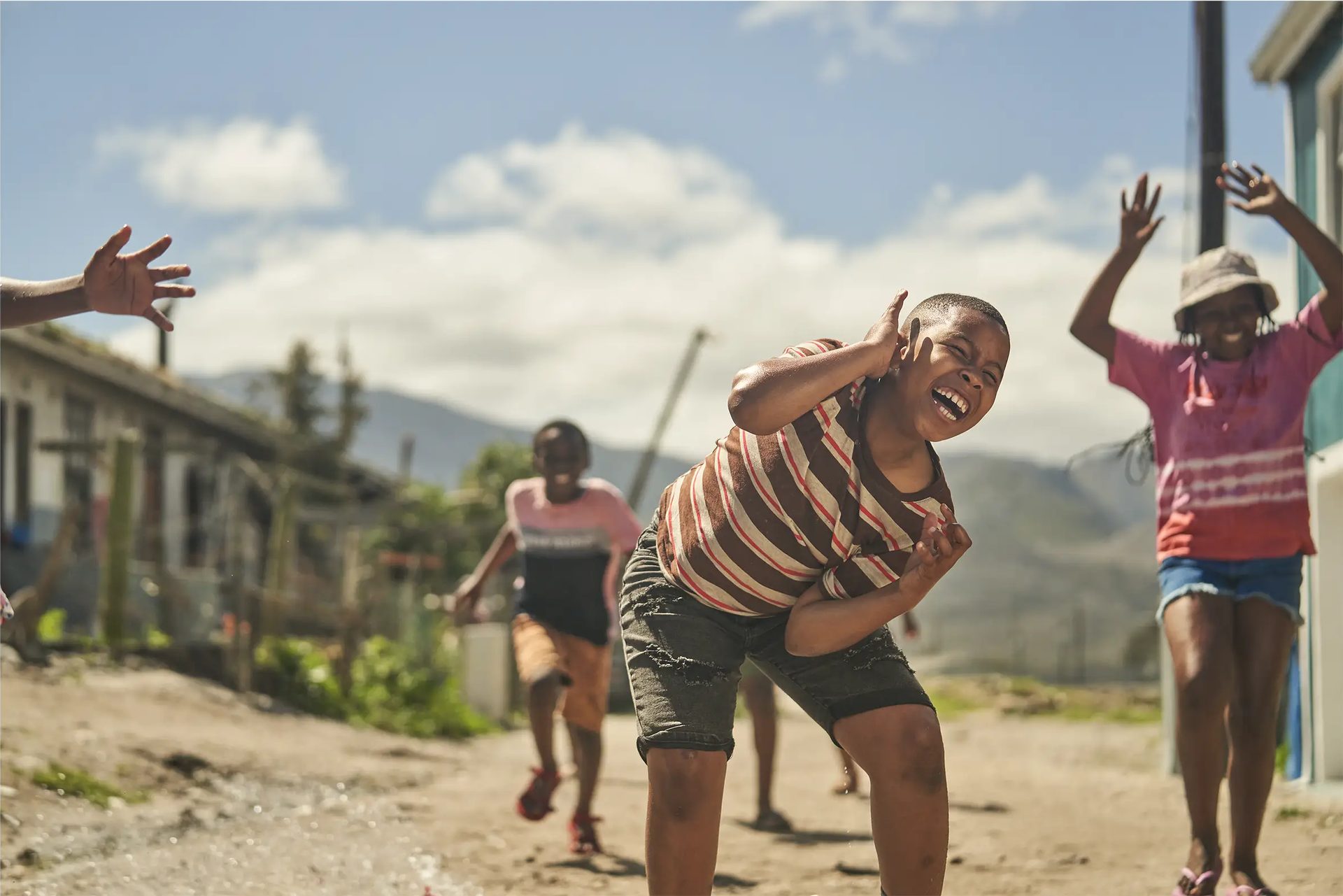 Original capture of children playing in a township street, boy ducking, dull hazy sky