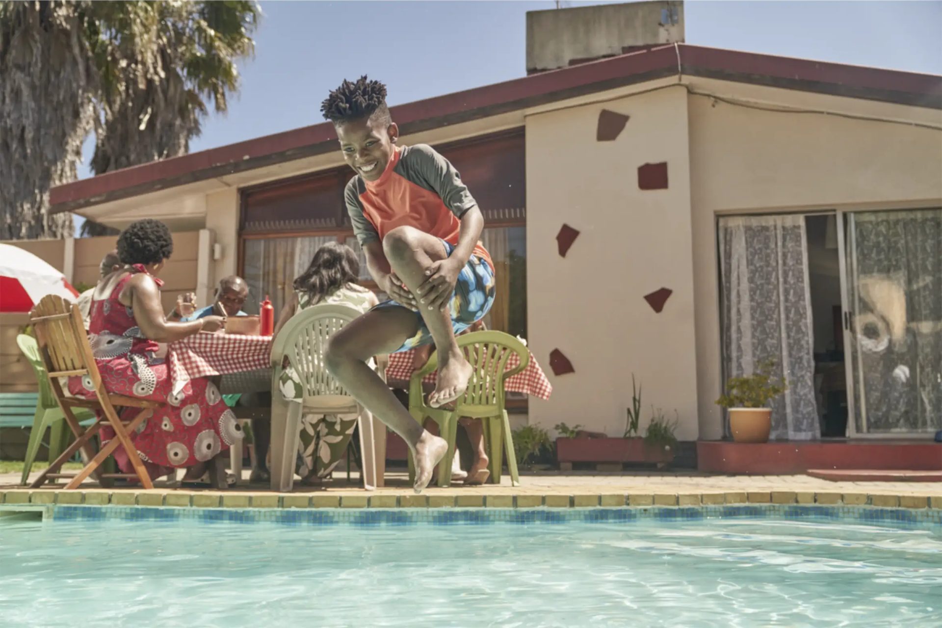 Original capture of a boy jumping into a backyard pool, no splash and flat afternoon light