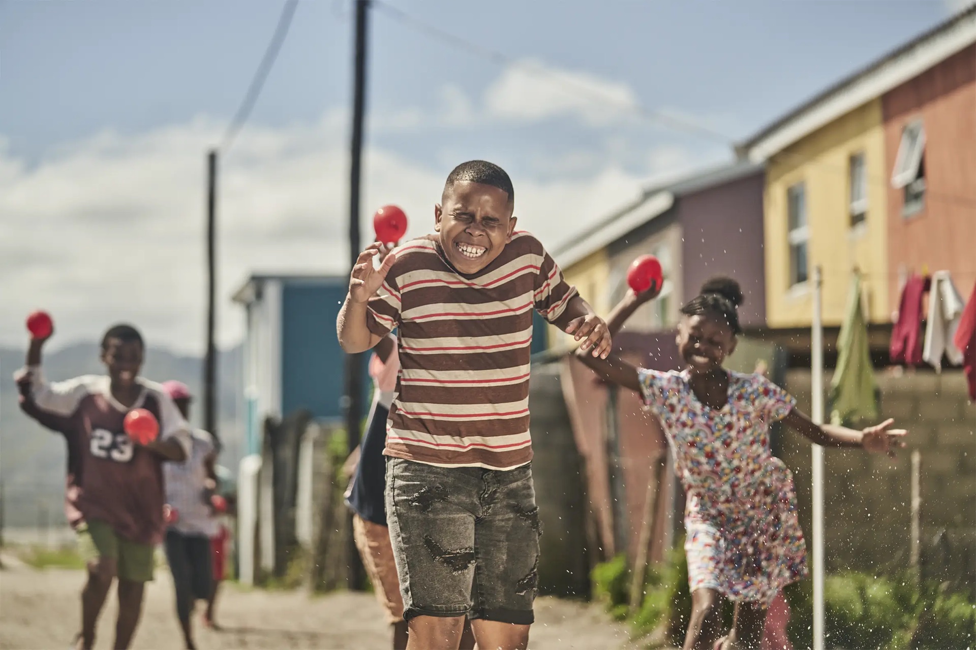 Original photograph of a boy grimacing mid water-balloon fight in a township street