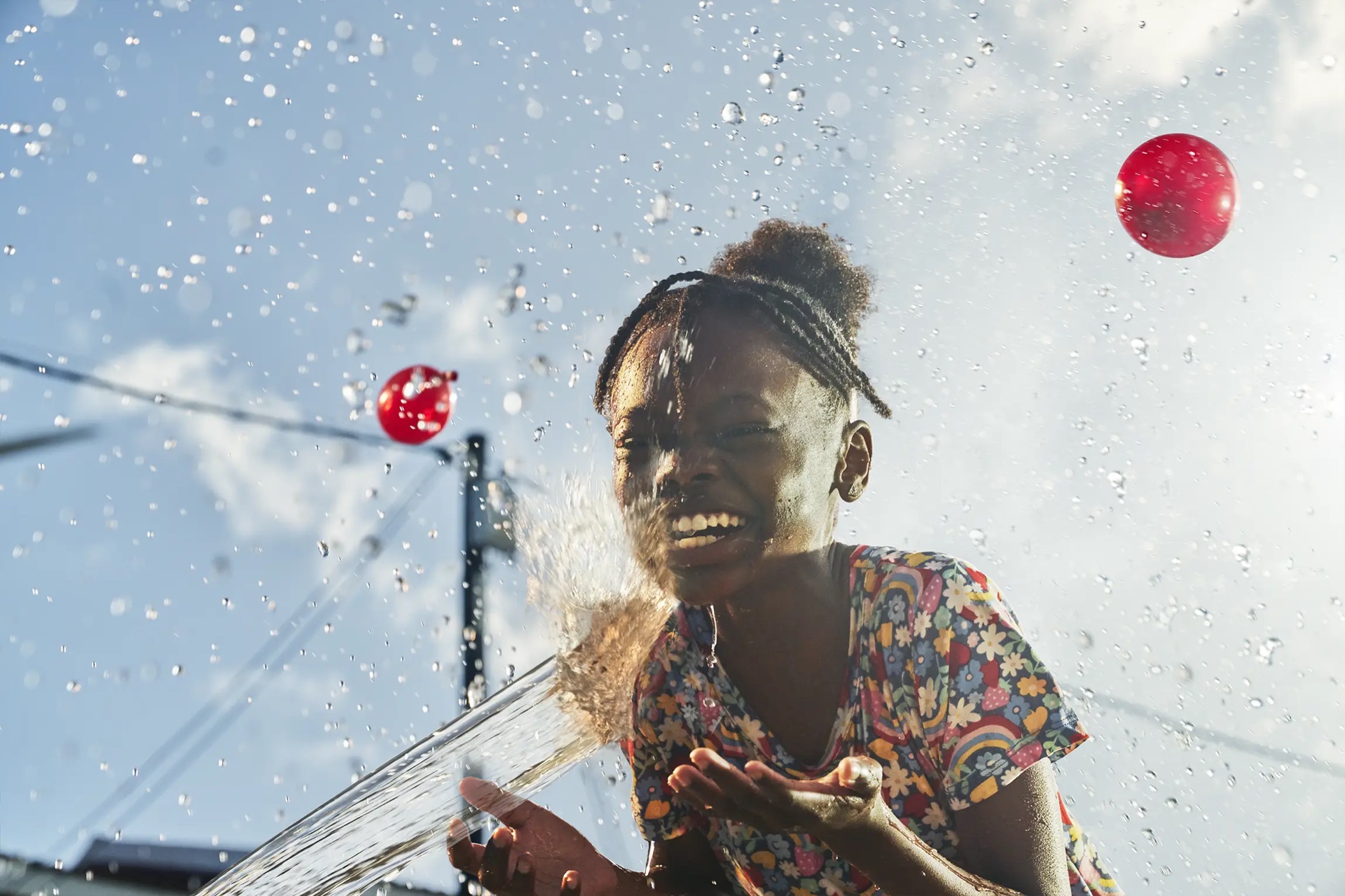 Finished artwork — blue sky, red water balloons and a burst of suspended droplets composited around her