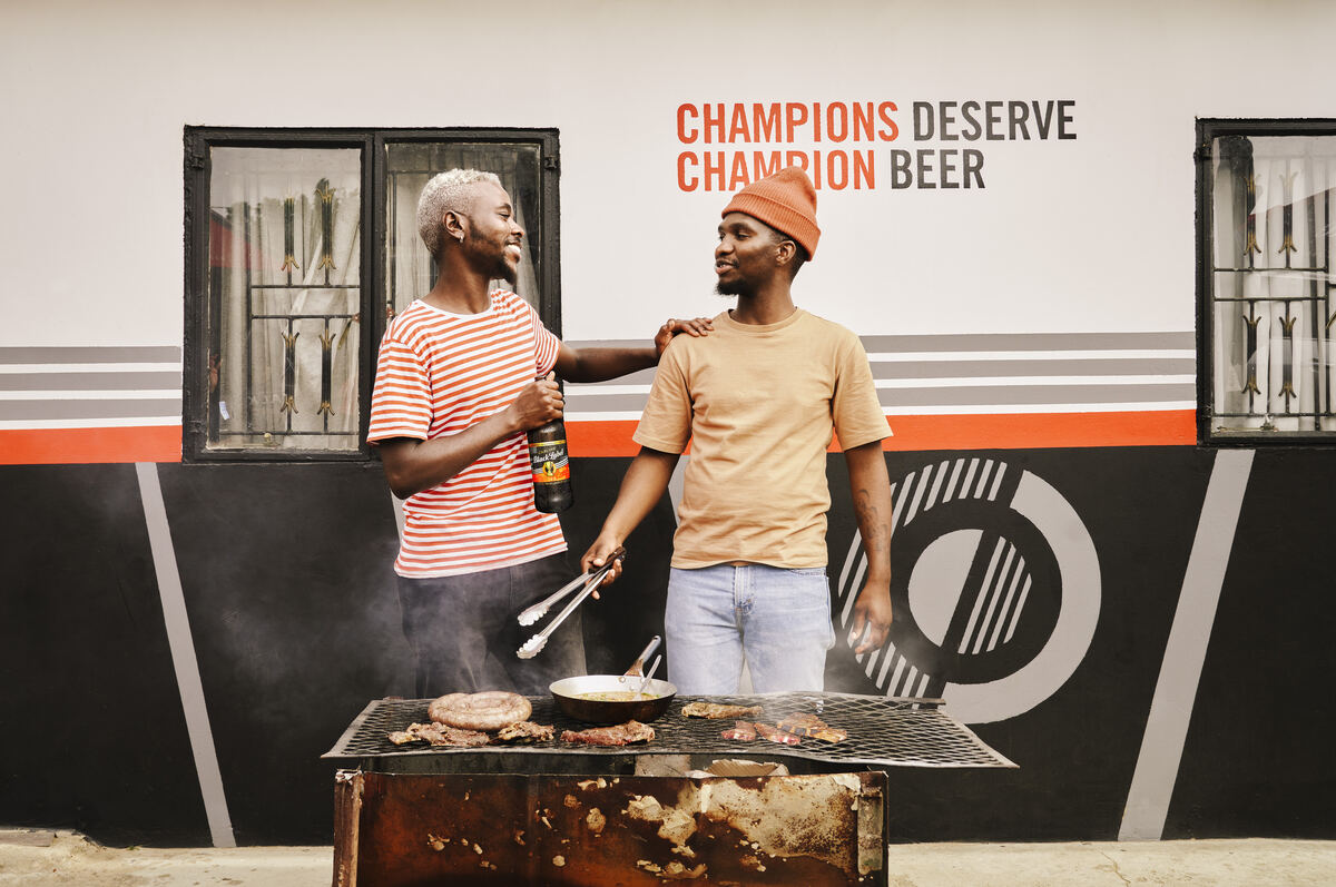 Friends sharing a beer at a braai in front of a Champions mural