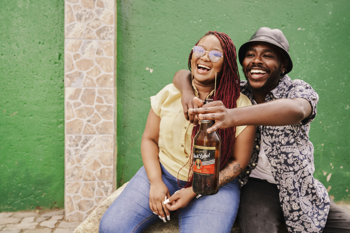 Laughing couple sharing a quart against a green township wall