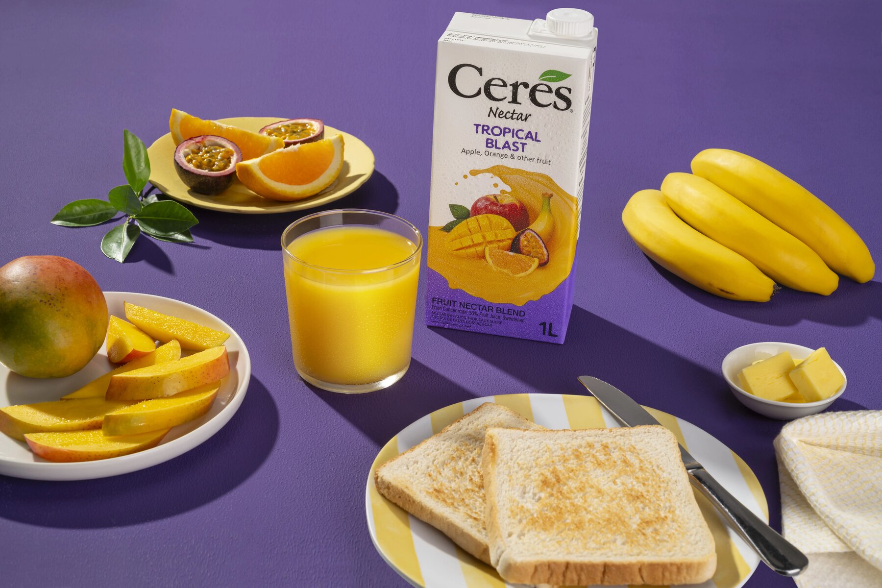 Ceres Nectar Tropical Blast carton styled on a breakfast table with toast, mango and fresh fruit