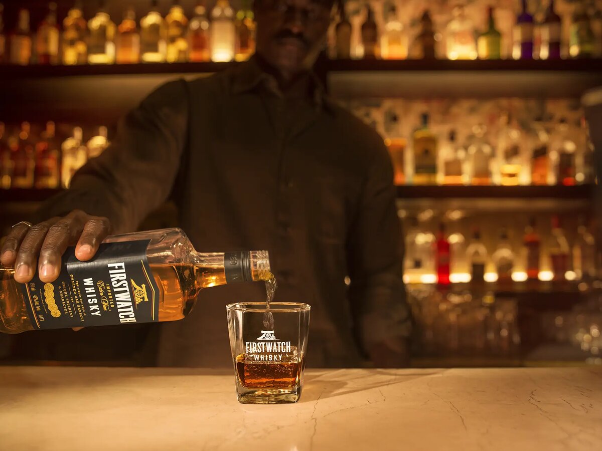Close-up of a hand holding a Firstwatch Whisky glass towards camera