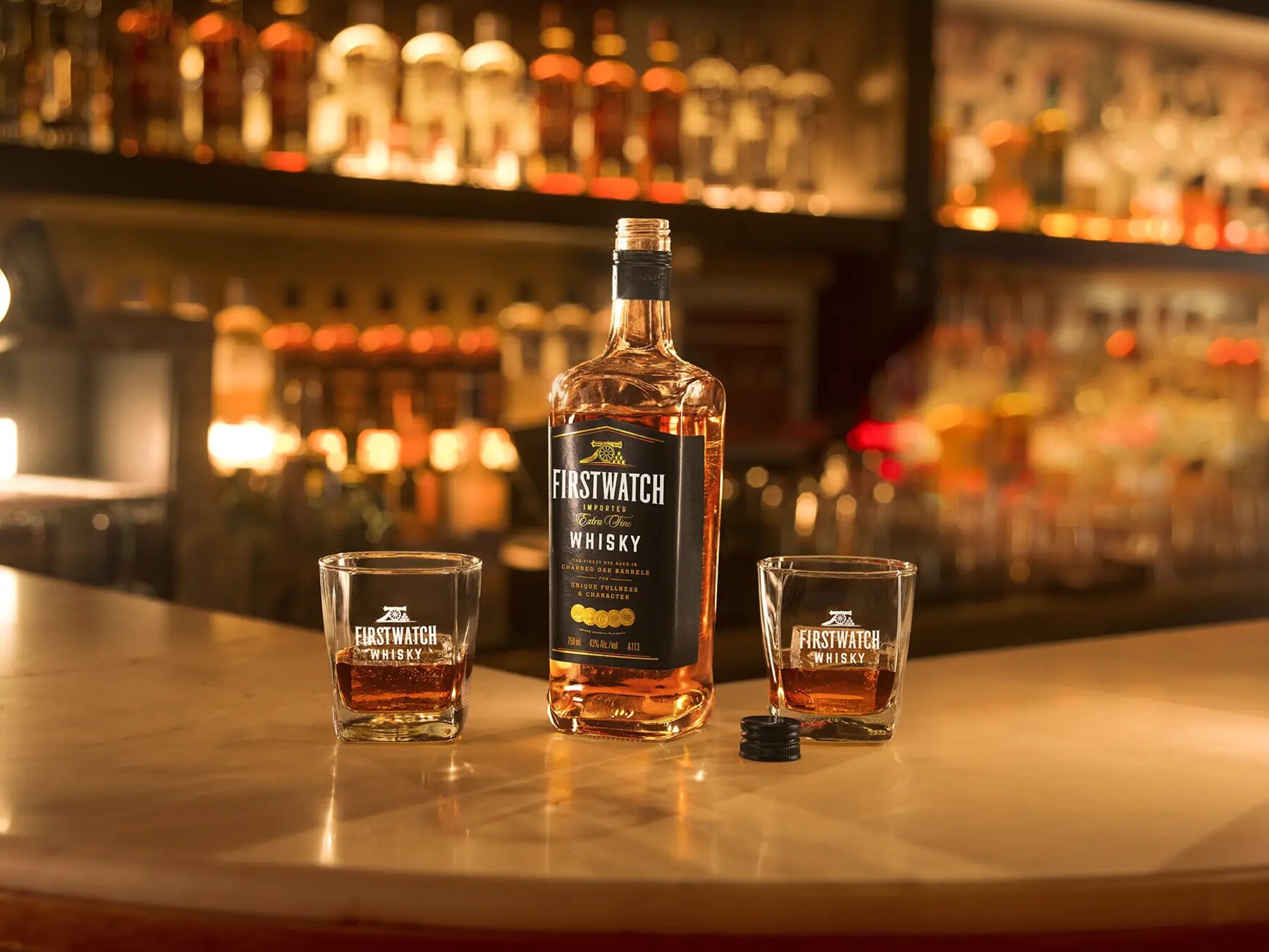 Firstwatch Whisky bottle between two branded glasses on a bar counter