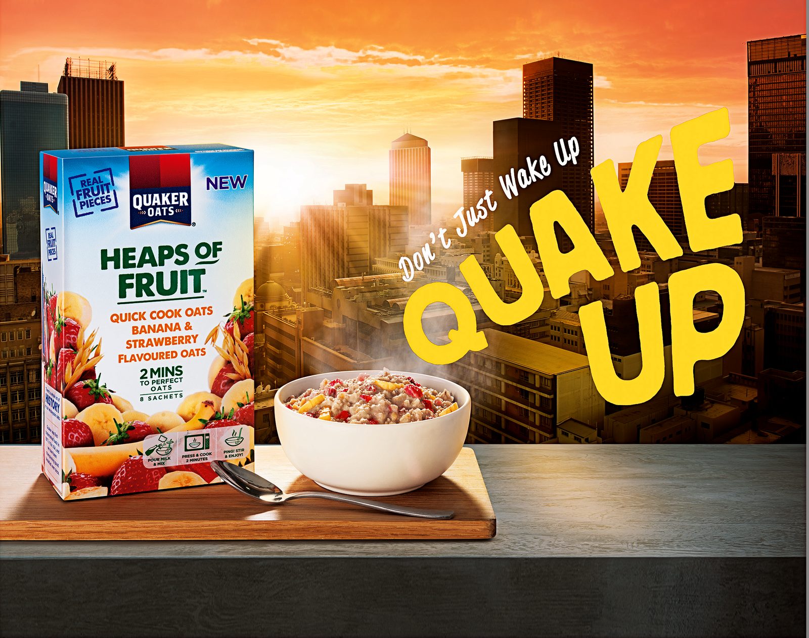 Quaker Oats Quake Up campaign artwork — Heaps of Fruit pack and steaming bowl against a sunrise city skyline
