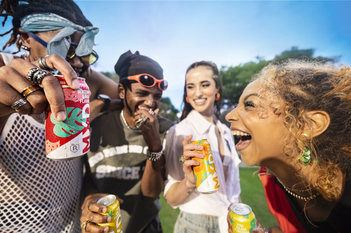Close-up of friends laughing together in a park, each holding an MXD spirit cooler can