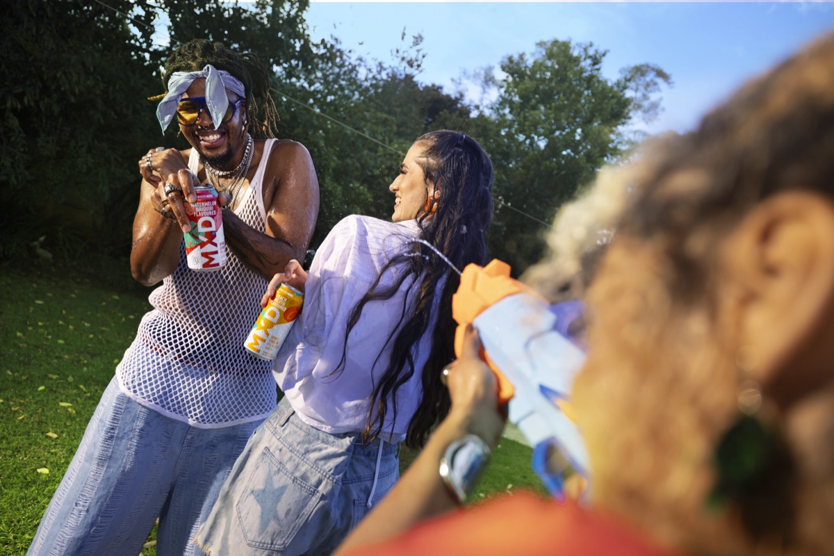 Friends holding MXD cans laughing in a garden water-pistol fight