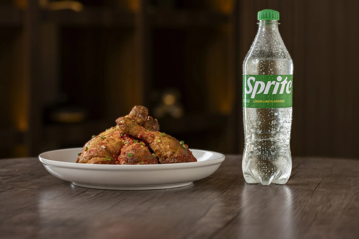 Sprite bottle beside a plate of pepper chicken on a wooden table