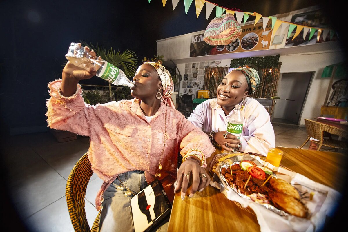 Two women drinking Sprite together at an outdoor food stand